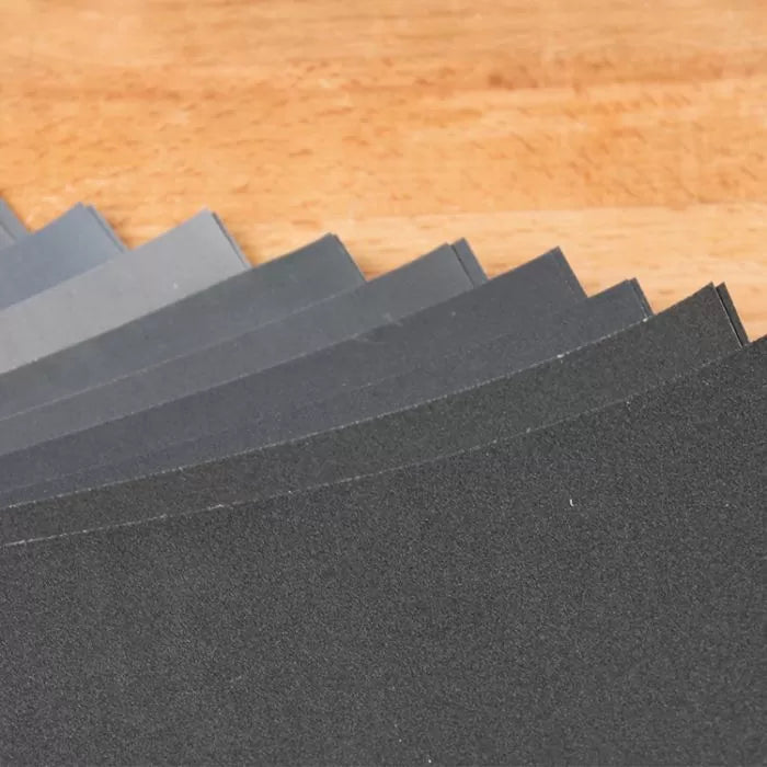 Assorted abrasive sandpaper sheets fanned out on a wooden surface for woodworking