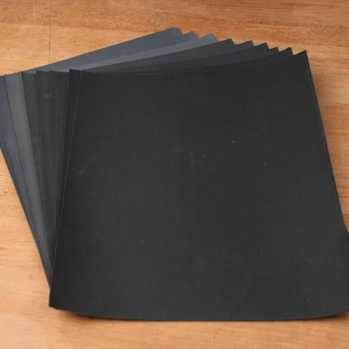 Assorted black and gray sandpaper sheets for woodworking on a wooden surface