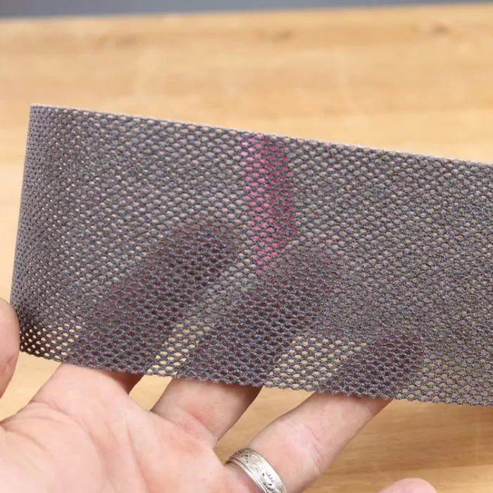 Hand holding mesh abrasive sanding strip over wood surface, woodworking tool accessory