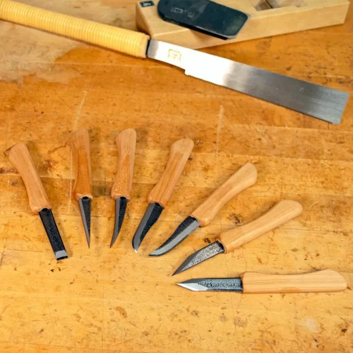 Set of woodworking carving knives with wooden handles and a detail saw on a workbench