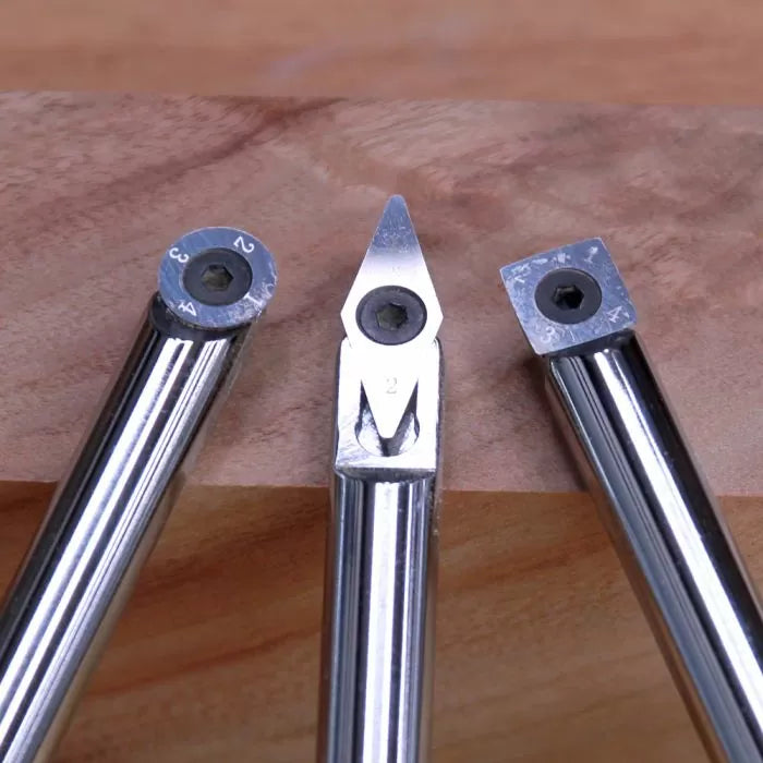 Set of three carbide woodturning tools with different cutter shapes on a wood surface