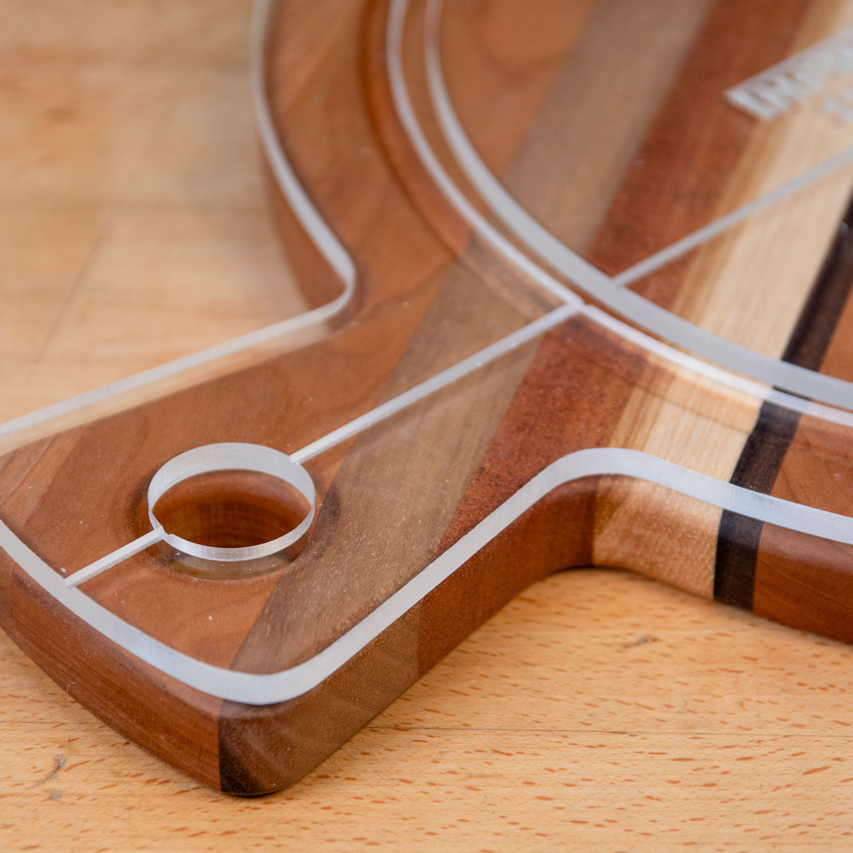 Closeup of acrylic cutting board template on a wood surface, showing routed edges and hole