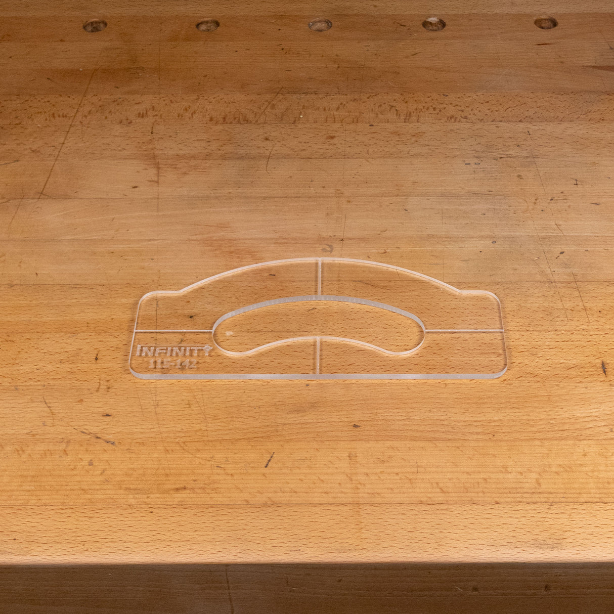 Clear acrylic handle template for woodworking placed on a wooden workbench.