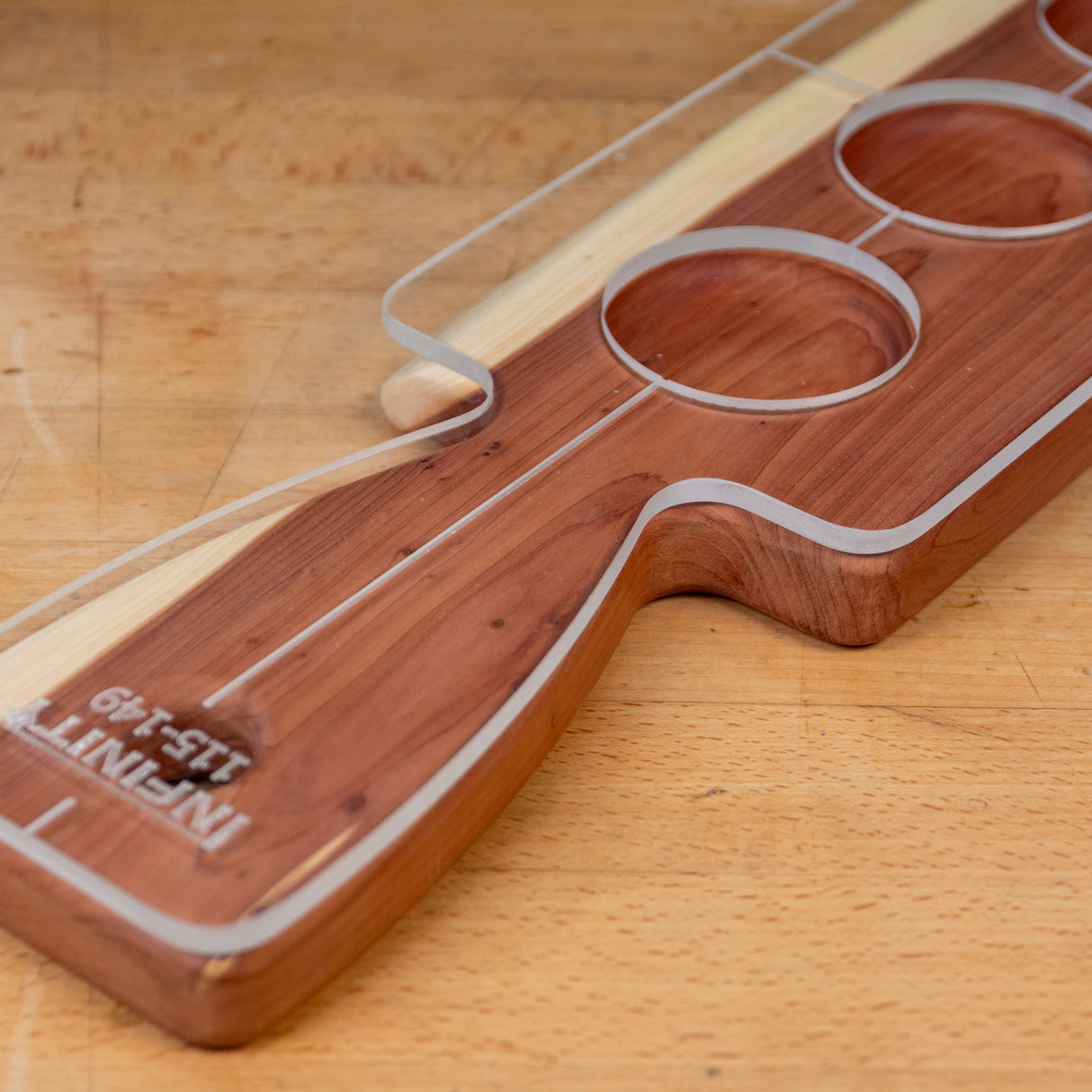 Acrylic cutting board template on hardwood paddle with circular cutouts, woodworking tool