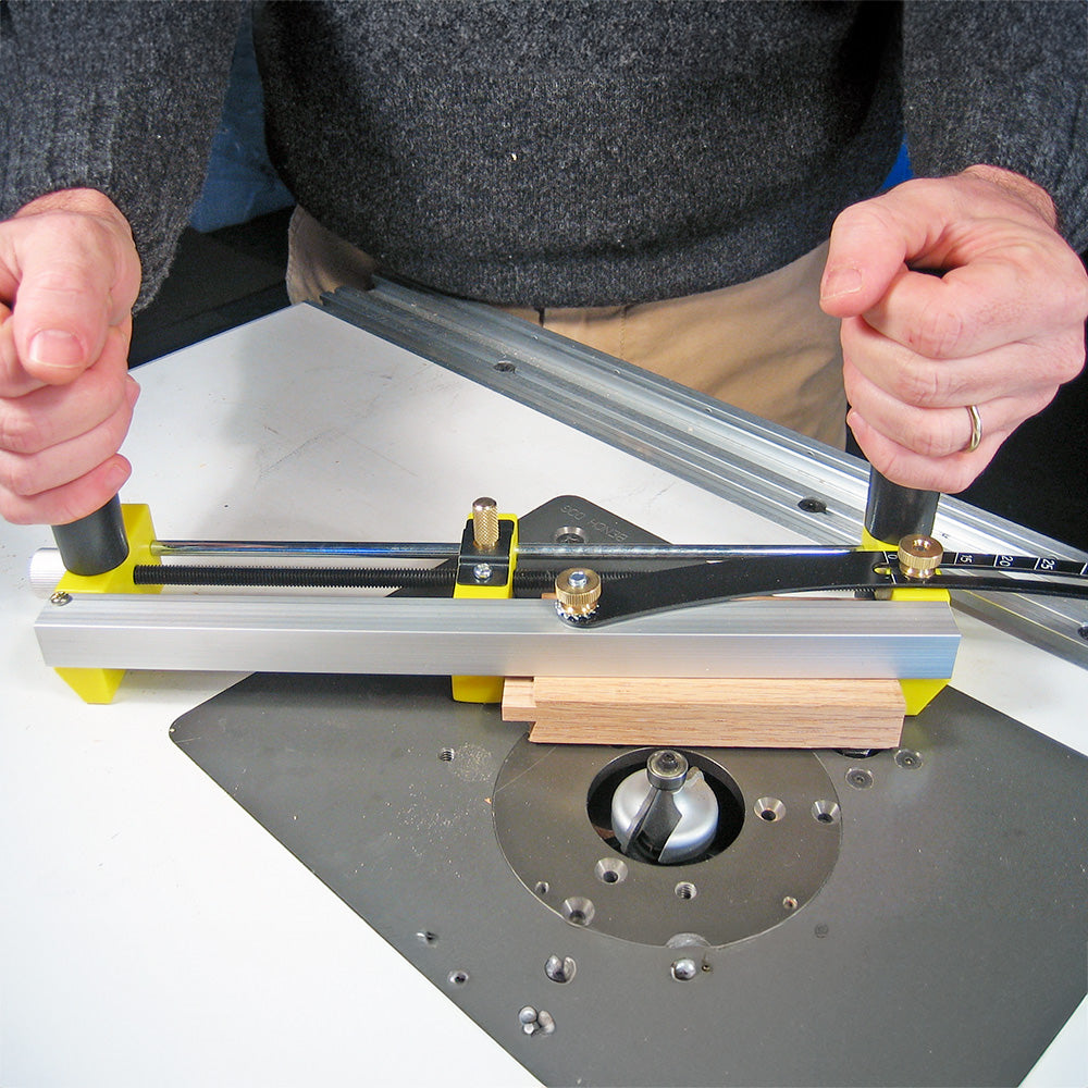Woodworker using a router table and adjustable jig to precisely guide wood piece