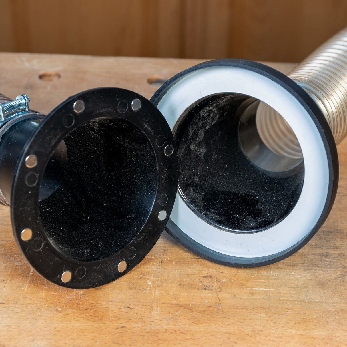 Magnetic dust collection hose coupling with black flanges on a wooden workbench