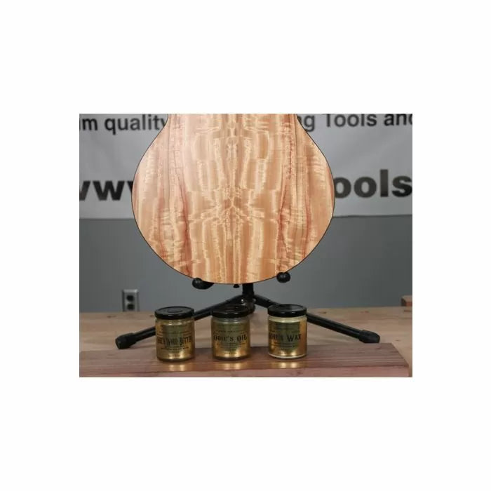 Curly maple guitar back with three jars of wood finishing oil and wax on a workbench.
