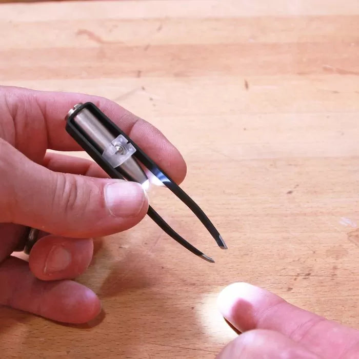 LED lighted tweezers held over a wooden workbench, hand reaching to use the tool