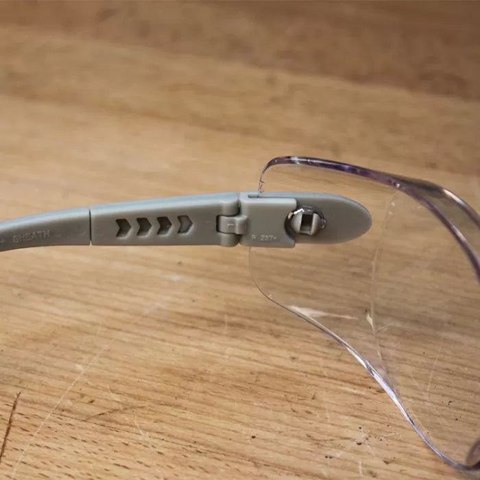 Clear safety glasses with gray adjustable arm on a wooden surface, woodworking safety gear