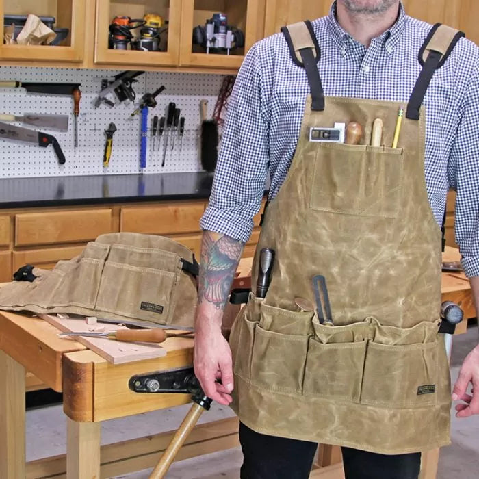 Woodworker wearing waxed canvas tool apron with pockets in a workshop setting.