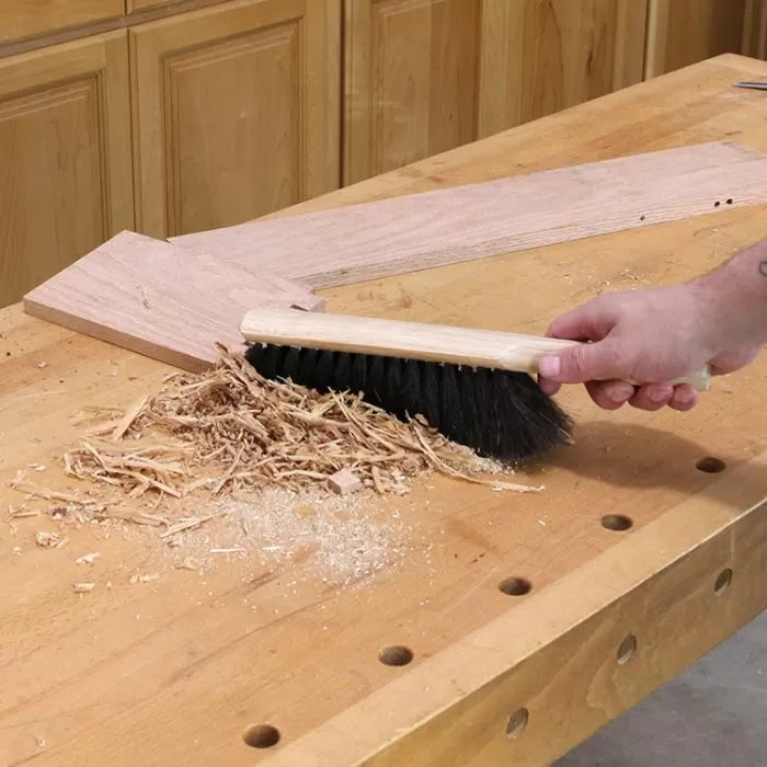 Hand sweeping wood shavings and sawdust off a woodworking bench with a brush