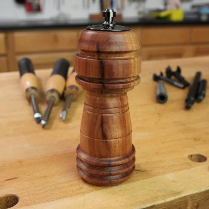 Woodturned pepper mill on a workbench with woodworking tools in the background