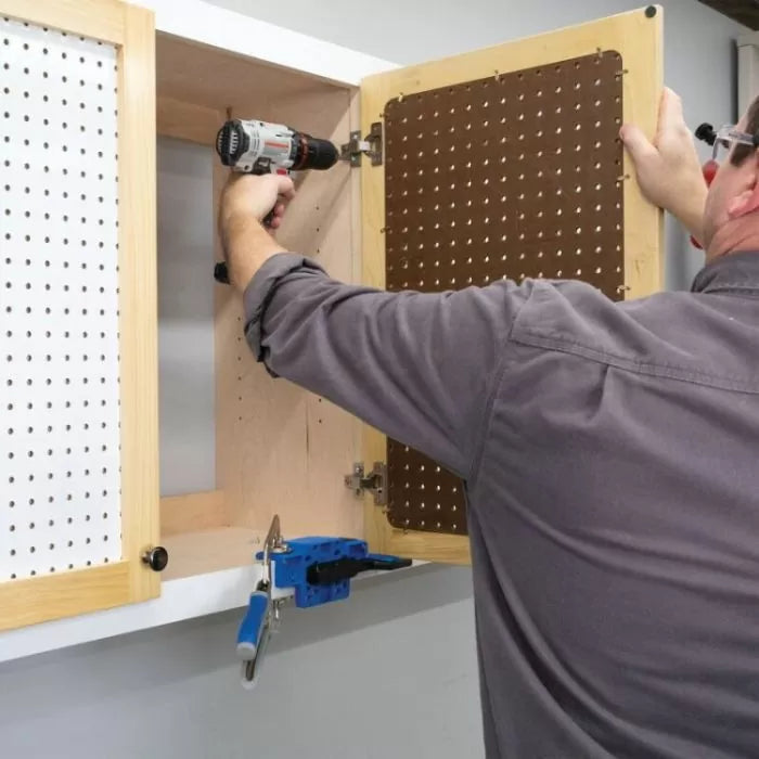 Person installing a pegboard cabinet using a power drill and woodworking clamp in workshop