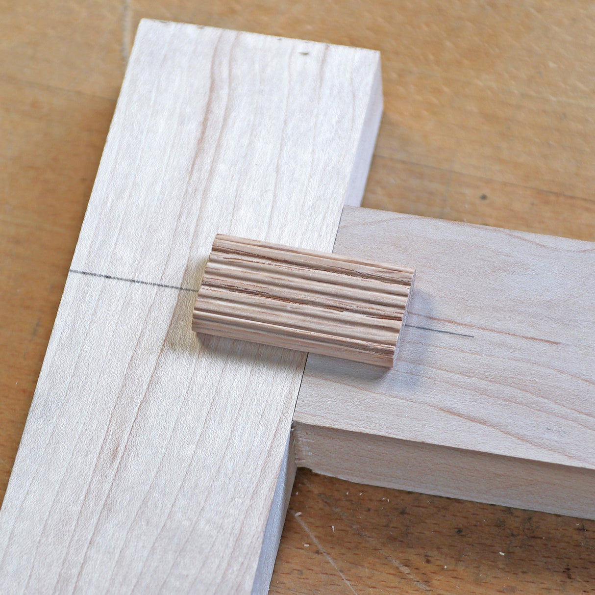 Woodworking dowel joint with fluted dowel connecting two pieces of wood on a workbench