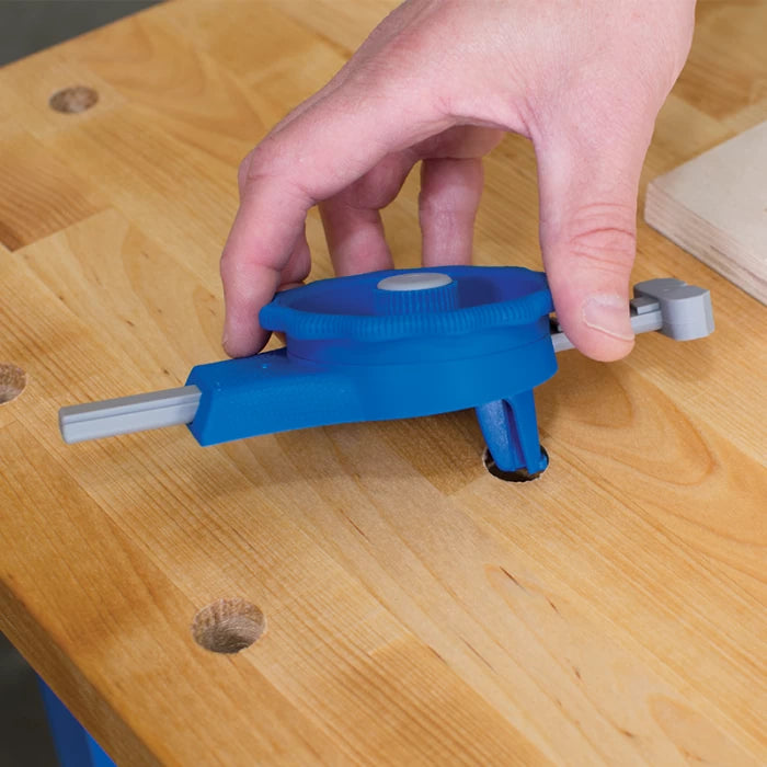 Hand adjusting blue woodworking jig tool on wooden workbench