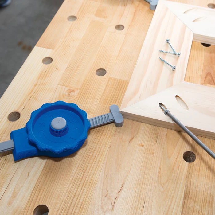 Woodworking clamp holding mitered wood pieces on workbench with screws and screwdriver