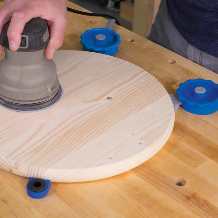 Hand sanding round wooden board held with blue woodworking bench clamps