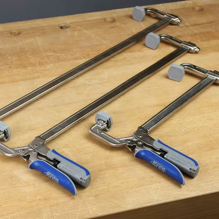 Three metal woodworking clamps with blue handles on a wooden workbench
