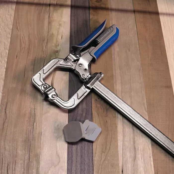 Metal woodworking clamp with blue handle and two clamp pads on wooden surface