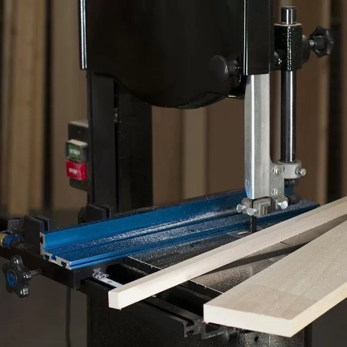Bandsaw cutting wood with blue fence in woodworking shop, precision saw accessory in use