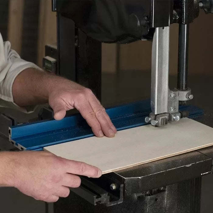 Woodworker guiding plywood through bandsaw with blue fence for precise cutting
