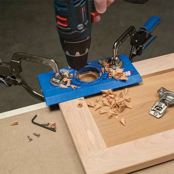 Drill with hinge jig clamped to cabinet door for precise woodworking and hinge installation
