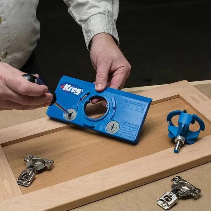 Person using Kreg cabinet hardware jig with screwdriver on wooden cabinet door, router bit nearby