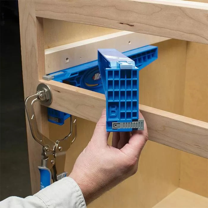 Hand using blue pocket hole jig with clamp on wood cabinet frame for woodworking