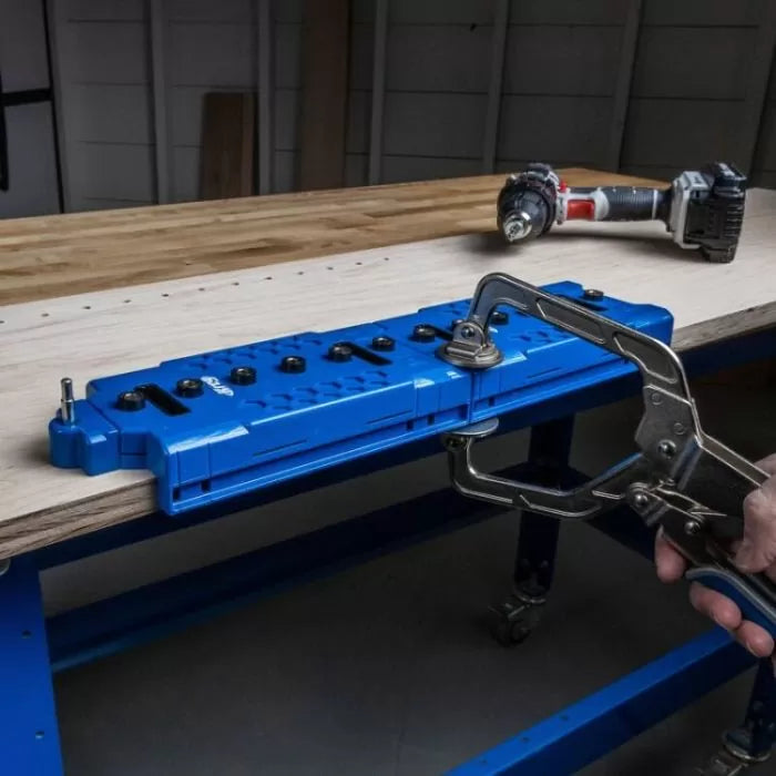 Blue pocket hole jig clamped to workbench for woodworking, cordless drill nearby