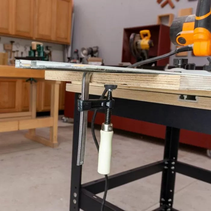 Woodworking table setup with a clamp securing plywood and power tool in a workshop.
