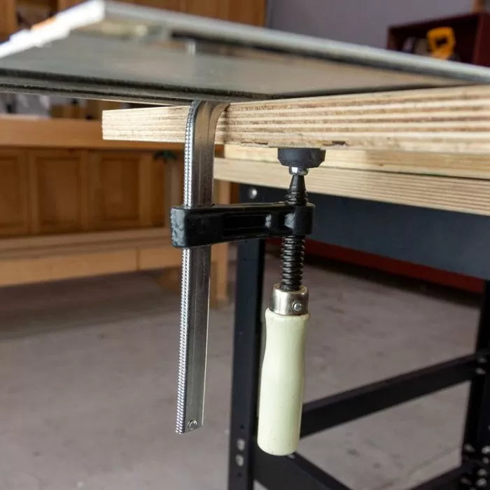 Steel woodworking clamp securing plywood on a workbench in a workshop setting