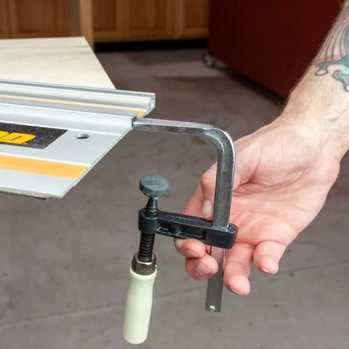 Woodworking track clamp securing guide rail to workbench with hand adjusting tool.