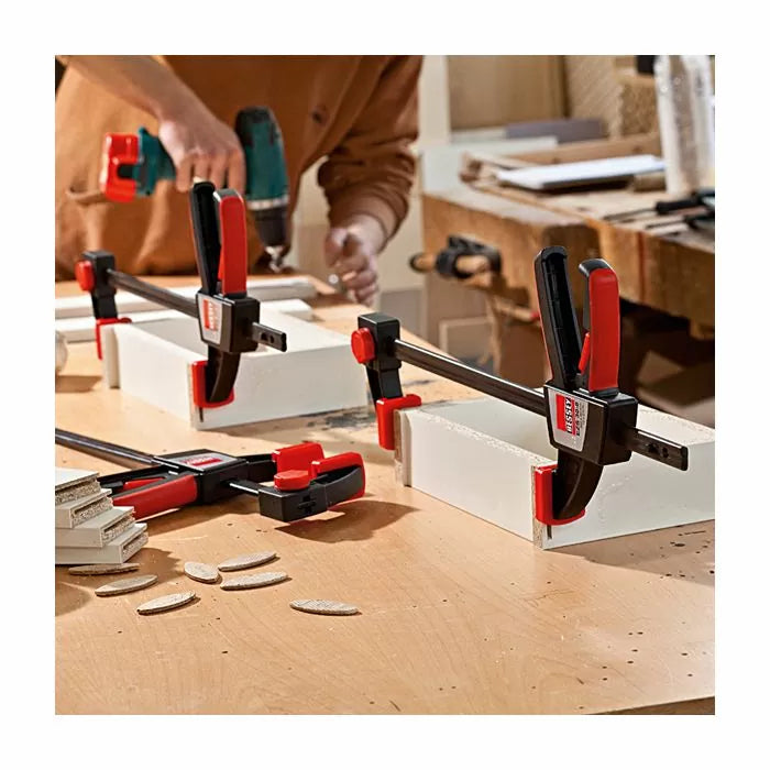 Woodworking bar clamps securing boards on a workbench with biscuit joinery visible.