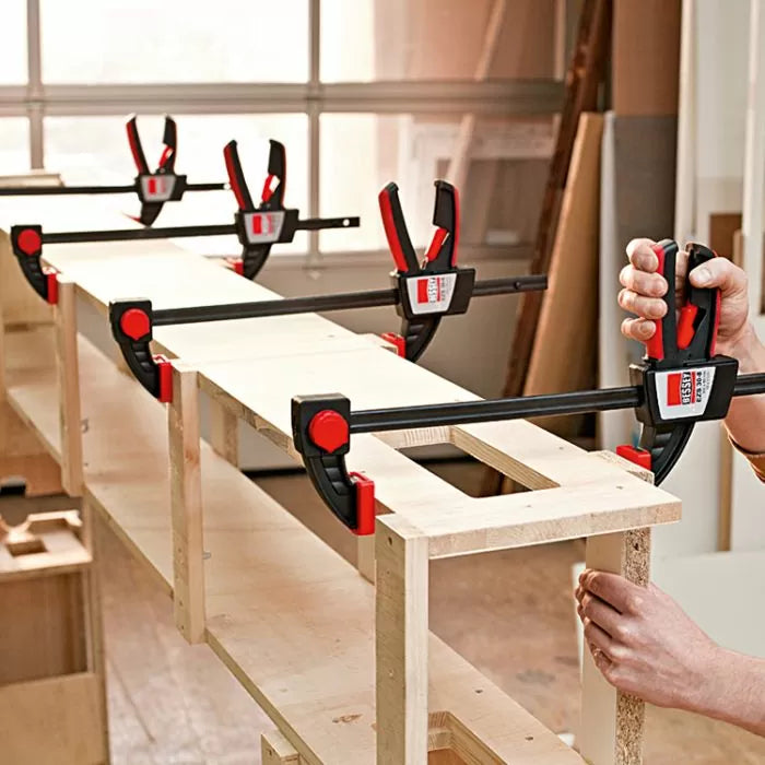Quick-release bar clamps securing wooden boards in a woodworking shop