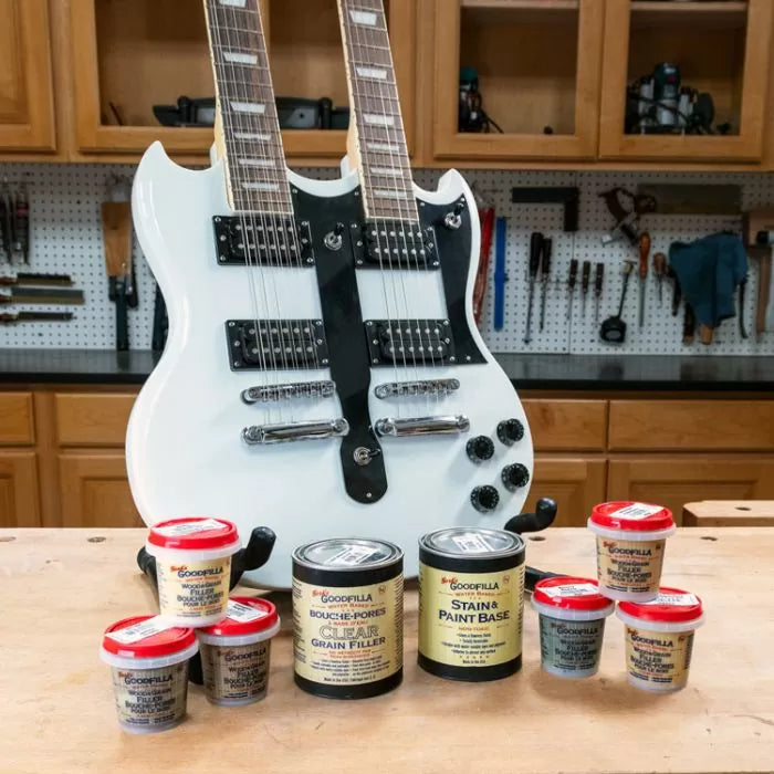 White double-neck electric guitar on workbench with wood filler and paint cans in woodworking shop