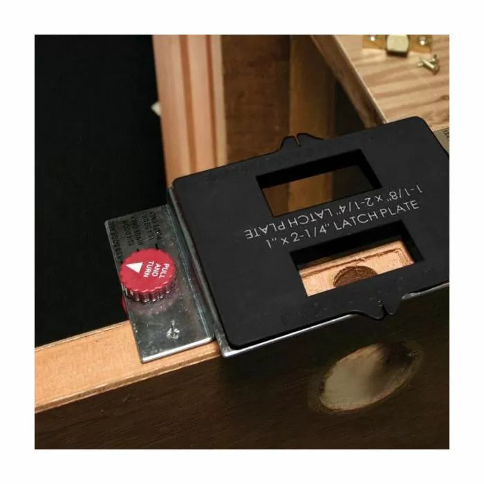 Woodworking door latch plate jig with metal template and adjustment knob attached to a door edge.