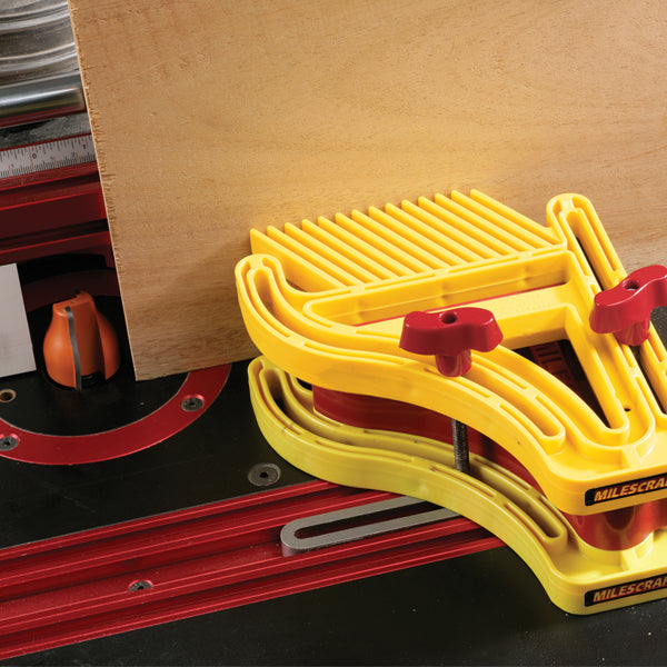 Router table with yellow featherboard holding plywood for woodworking precision