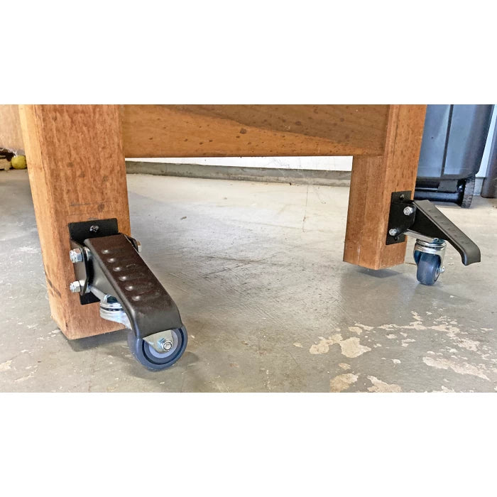 Heavy-duty workbench casters with foot levers attached to wooden legs on workshop floor