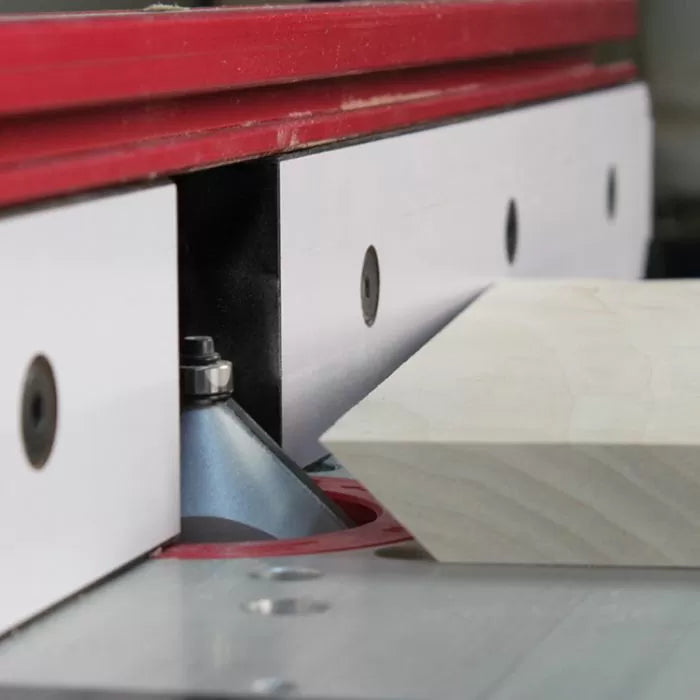 Router table with chamfer bit shaping a wood board, woodworking tool close-up