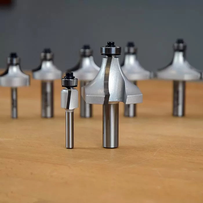 Assorted carbide-tipped router bits with bearings on a wooden surface, woodworking tool set.