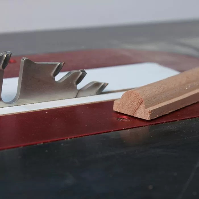 Table saw blade with custom profile next to shaped wooden molding on work surface