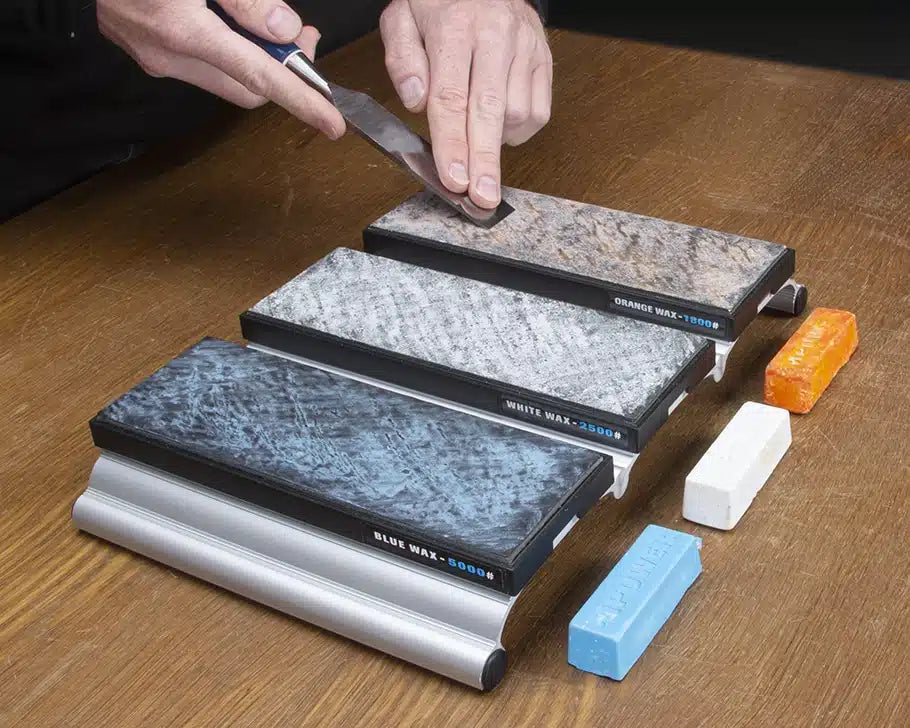 Hand sharpening a chisel on a set of marble honing stones with colored wax bars on table