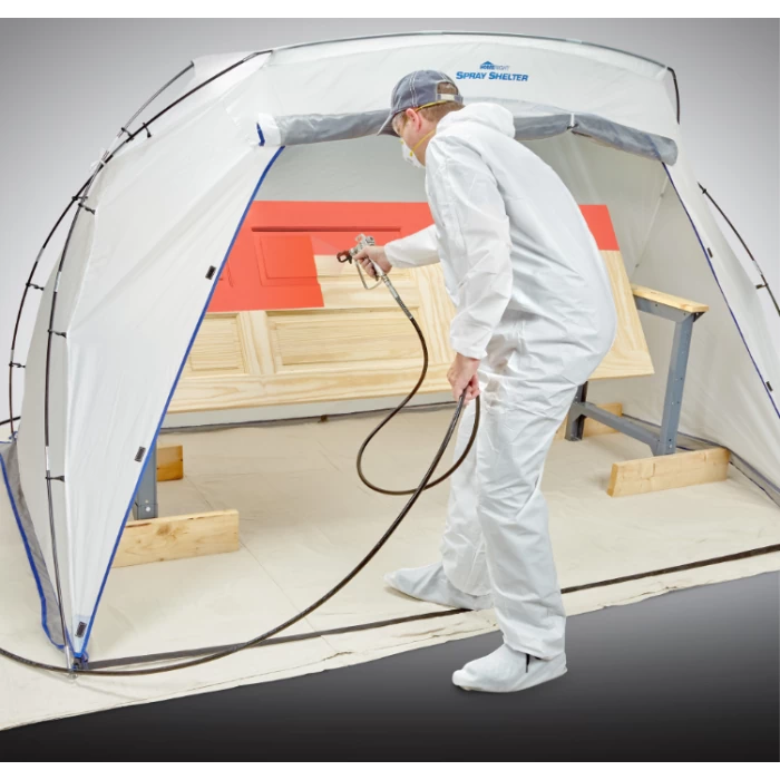 Person spray painting wood panels in a portable spray shelter for woodworking projects.