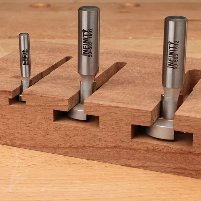 Three straight router bits cutting grooves in a wooden board on a workbench