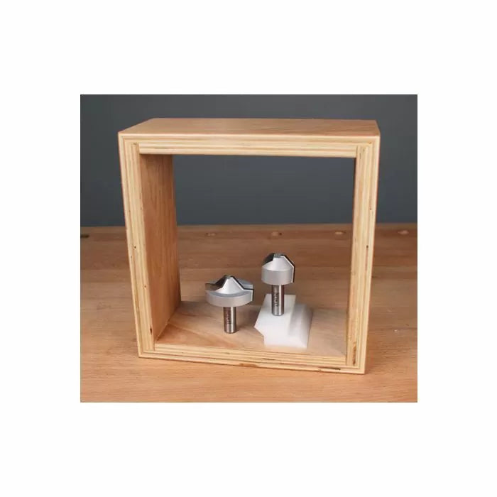 Two carbide-tipped router bits displayed inside a wooden frame on a workbench