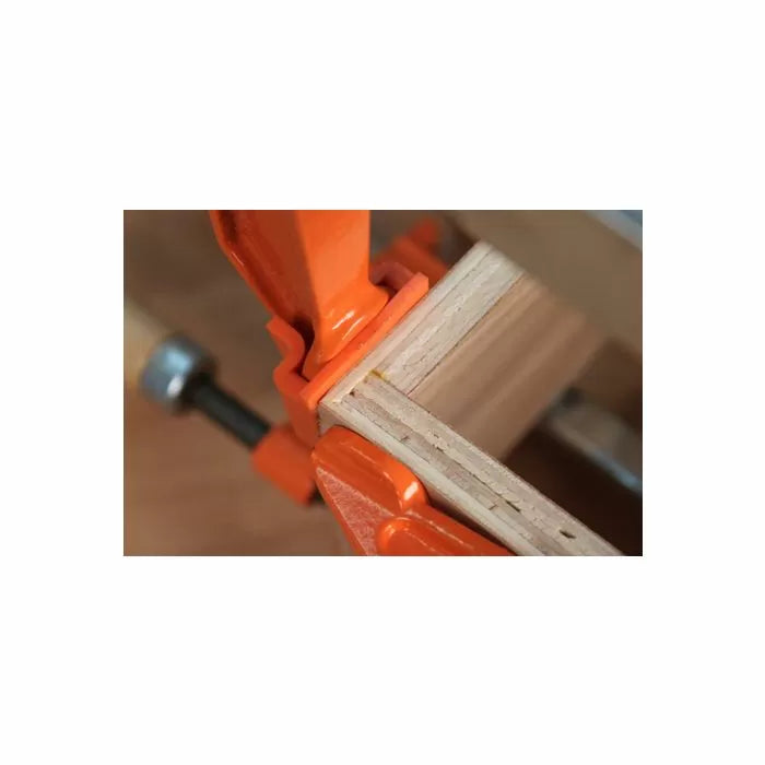 Woodworking corner joint clamped with an orange bar clamp on a workbench