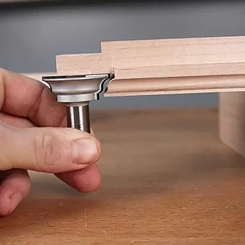 Hand holding roundover router bit next to shaped edge of wooden board on workbench