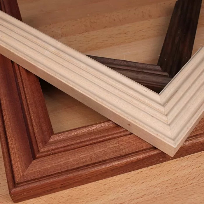 Three mitered wood picture frame corners in different finishes on a workbench