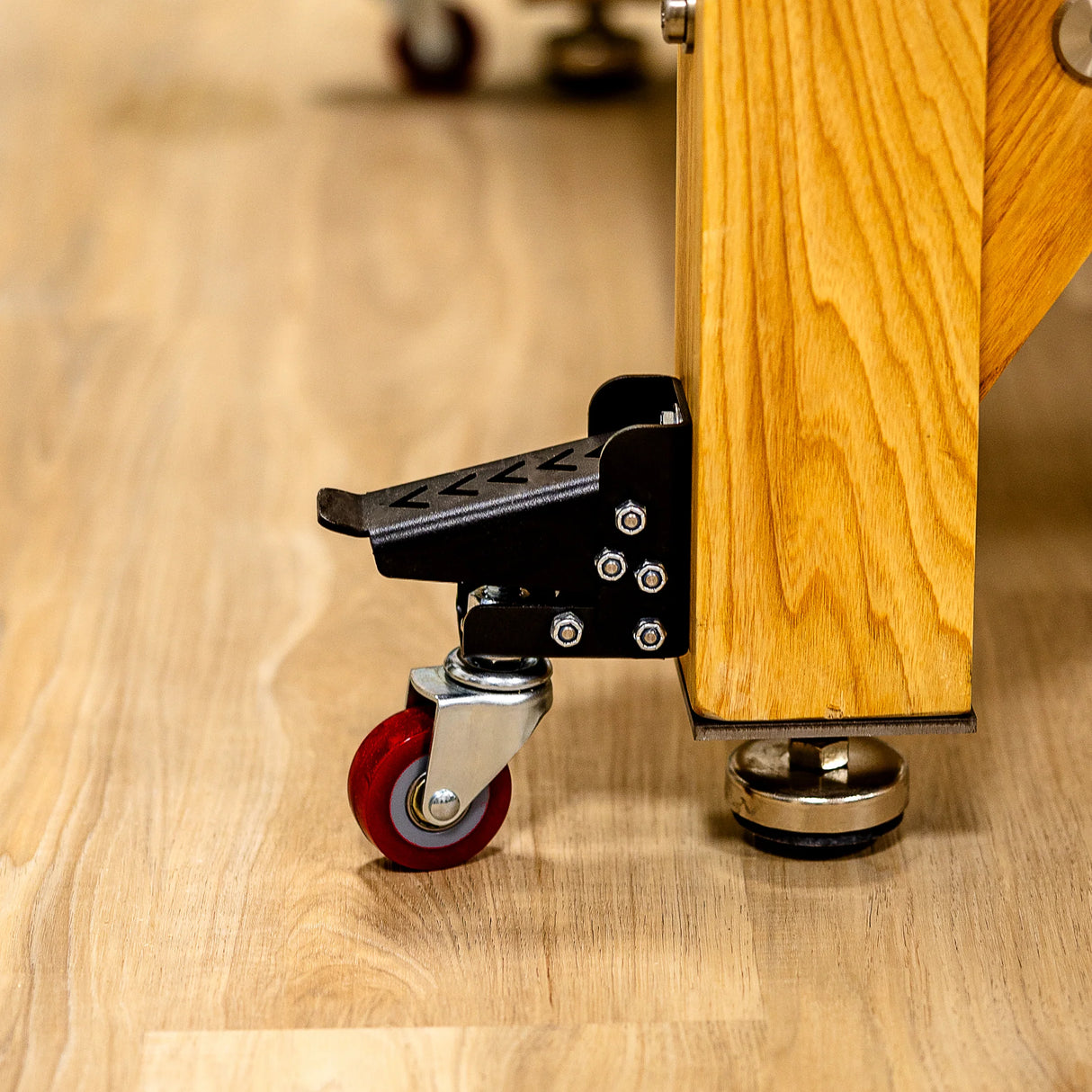 Workbench caster wheel with foot pedal attached to wooden leg on hardwood floor, woodworking tool accessory