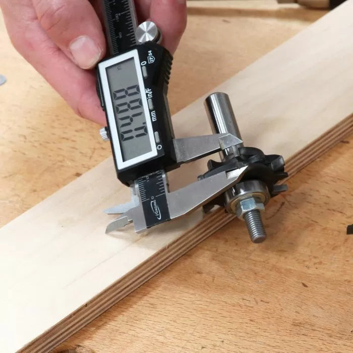 Digital caliper measuring woodworking router bit on plywood workbench
